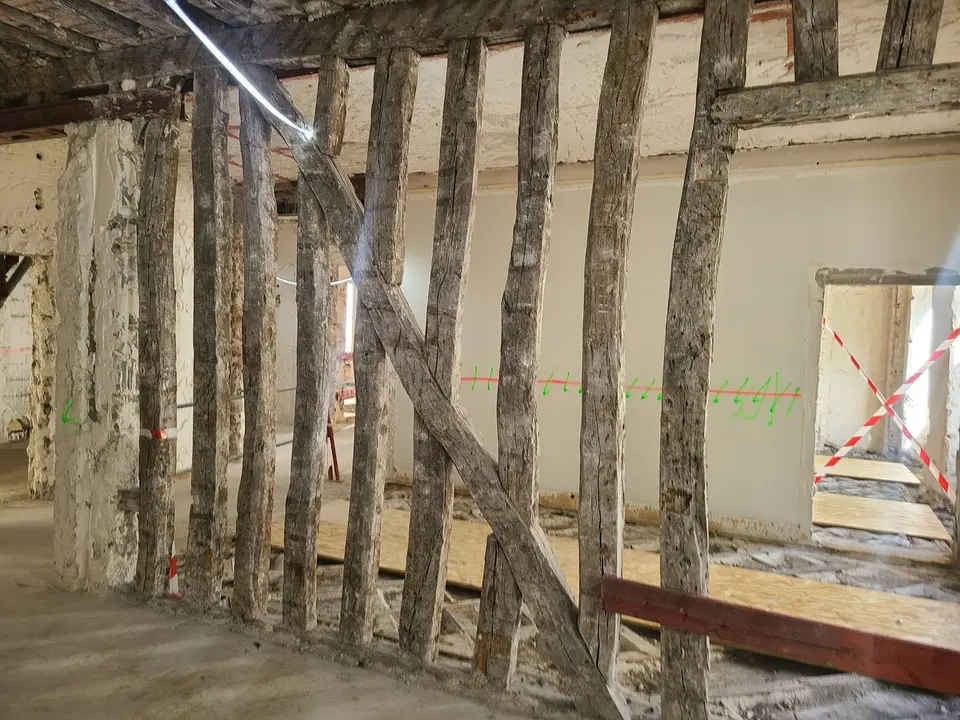 Pan de bois — mur de refend existant mis à nu. Structure en poteaux/décharges bois datant du 19ᵉ siècle, à caractériser et renforcer.