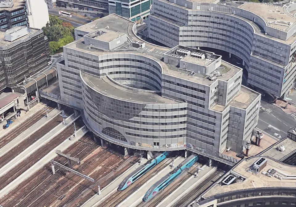 Vue aérienne du bâtiment existant — immeuble à géométrie courbe posé directement sur les voies de la Gare Montparnasse