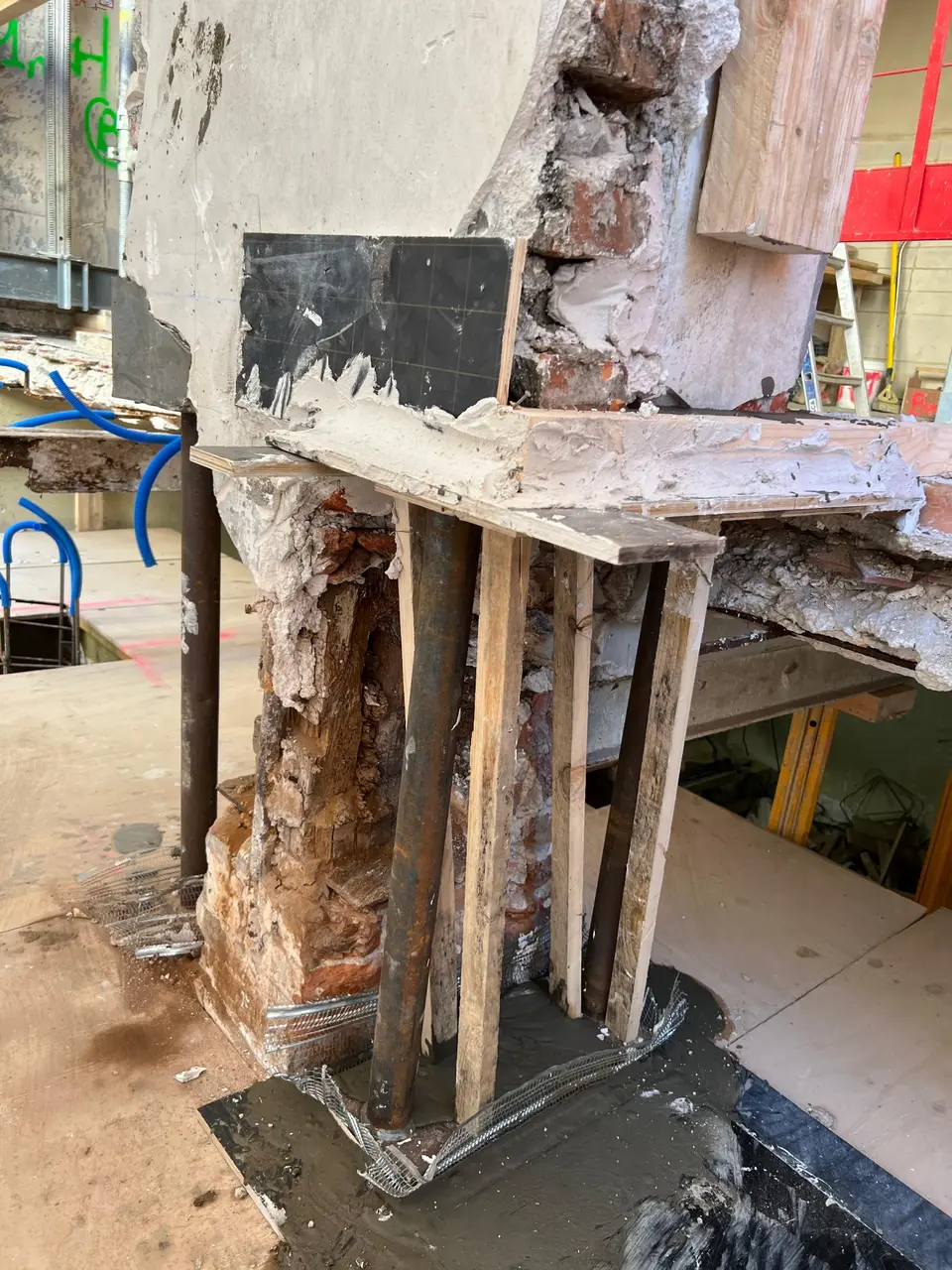 Tabouret provisoire — trumeau maçonnerie brique/pierre suspendu sur 4 tubes acier avec platine de répartition, en attente de reprise en sous-œuvre définitive.
